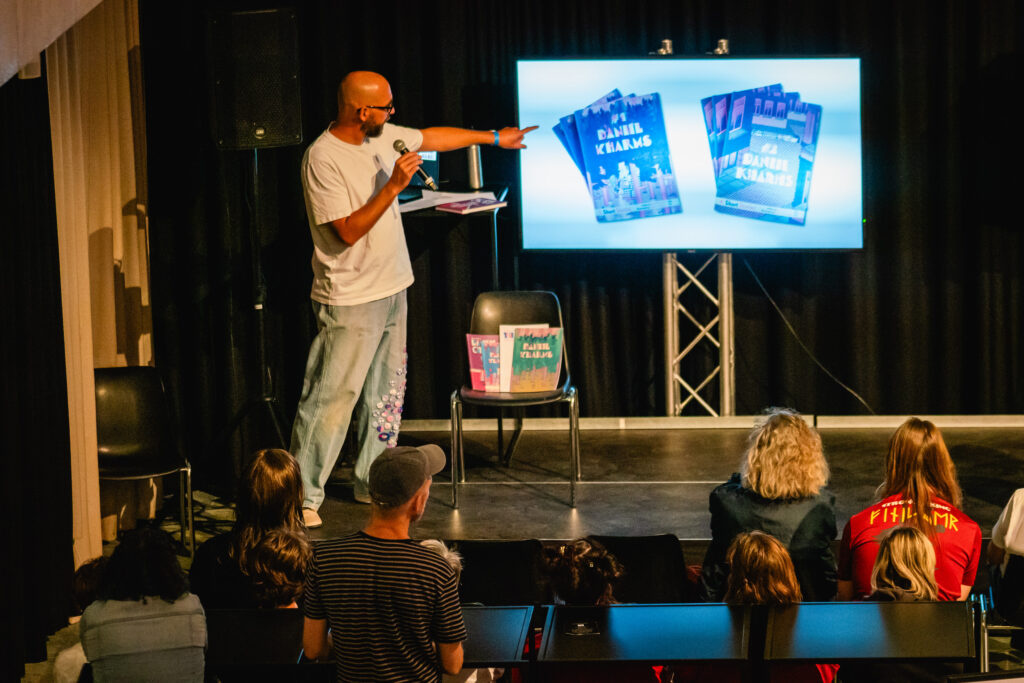 A man is standing in front of a screen and pointing at a picture of his book. A crowd is watching.
